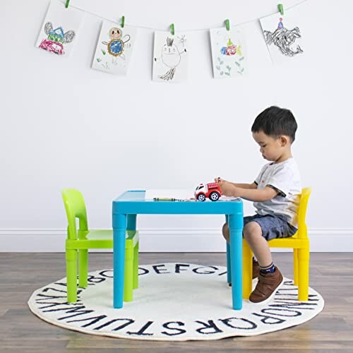 Child sitting at a small table with drawings hanging above.